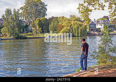 Angler, pêche sur les rives de la Tamise près de Teddington avec maisons cossues sur loin de la banque. Banque D'Images