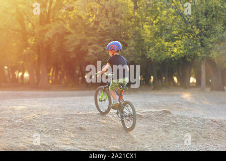 Happy kid garçon de 7 ans s'amuser dans le parc de l'automne avec un vélo sur belle journée d'automne. Casque de vélo enfant portant Active Banque D'Images