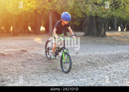 Happy kid garçon de 7 ans s'amuser dans le parc de l'automne avec un vélo sur belle journée d'automne. Casque de vélo enfant portant Active Banque D'Images