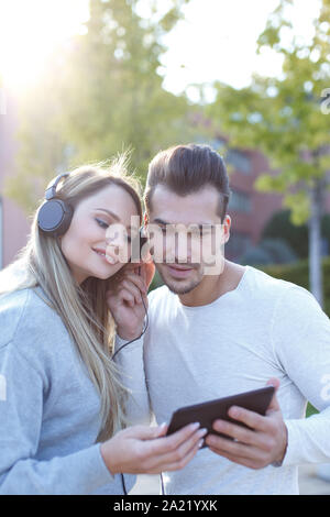 Jeune couple listening music par comprimé et d'écouteurs, de la technologie sans fil, écouteurs partage Banque D'Images