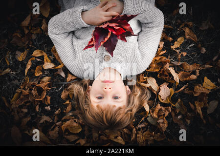 Petite fille est posée sur le sol et la tenue des feuilles de l'automne rouge Banque D'Images