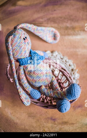 Un lapin tricoté en pastel est assis dans un panier en vigne. Vintage photo de jouets faits à la main. Banque D'Images