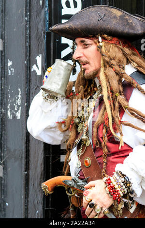 Jour pirate dans Hastings, Royaume-Uni. Homme mûr habillé en pirate avec de longs cheveux tressés, en prenant un verre de bière silver tankard. Vue de côté. Close up. Banque D'Images