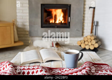 Hygge concept avec livre ouvert et tasse de thé près de cheminée à bois Banque D'Images