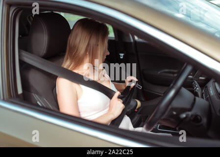 Girl intérieur de voiture appelle sur le téléphone, regarde dans le rétroviseur intérieur, les parcs de stationnement de centre commercial, c'est attaché par volant. Femme en Banque D'Images