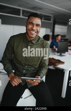 Portrait of a smiling young woman holding digital tablet in part à la recherche d'appareil photo et collègue au contexte Banque D'Images