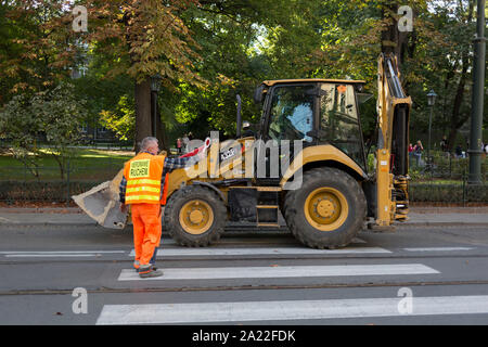 Un travailleur de la construction de la route de la circulation s'arrête comme un tracteur roulant à l'avant des voitures sur une rue dans le centre de Cracovie, le 23 septembre 2019, à Cracovie, Pologne, Malopolska. Banque D'Images