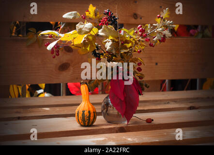 Bouquet d'automne avec feuilles jaunes et rouges, baies de forêt, citrouille décorative et vase en verre Banque D'Images