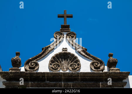 Triangle de la toiture d'une église avec des bords et une croix. Façade blanche. Ciel bleu. Ribeira Grande, São Miguel, Açores, Portugal. Banque D'Images