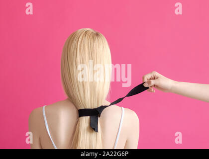 La coiffure beauté concept Woman's hand est déliée le ruban noir sur les cheveux de la femme blonde sur fond rose Banque D'Images