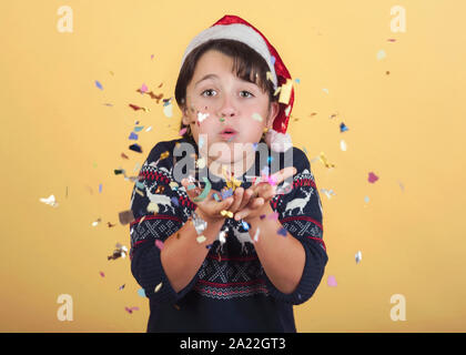 Soufflage enfant confetti Wearing Christmas Santa Claus Hat sur fond jaune Banque D'Images