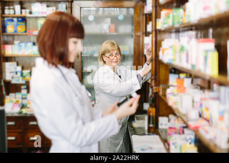 Young female pharmacist in pharmacy la lecture de l'information sur les médicaments. Femme blonde d'âge moyen pharmacien choisir le médicament sur le Banque D'Images