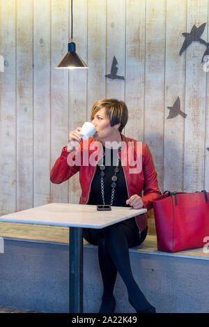 Femme élégante avec veste rouge assis dans un café boire du café. Banque D'Images
