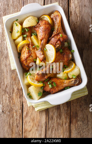 Les cuisses de poulet avec du citron et des pommes de terre à la sauce à l'ail en close-up dans un plat allant au four, sur la table. Haut Vertical Vue de dessus Banque D'Images