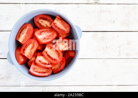 Produits frais bio tomates Roma ou réduit de moitié dans un bol en plastique bleu sur fond blanc patiné. Concept de saine alimentation. Mise à plat avec prix Banque D'Images