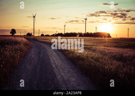 Paysage avec chemin de terre à travers champs avec wind turbine in rural area pendant le coucher du soleil Banque D'Images