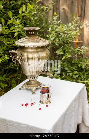 Samovar en cuivre vintage dans un porte-gobelet et un verre de thé chaud est sur la table recouverte d'une nappe blanche sont dispersés à côté de cerise et rasp Banque D'Images