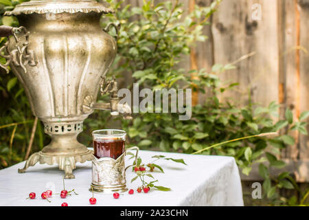 Samovar en cuivre vintage dans un porte-gobelet et un verre de thé chaud est sur la table recouverte d'une nappe blanche sont dispersés à côté de cerise et rasp Banque D'Images