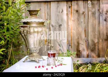 Samovar en cuivre vintage dans un porte-gobelet et un verre de thé chaud est sur la table recouverte d'une nappe blanche sont dispersés à côté de cerise et rasp Banque D'Images