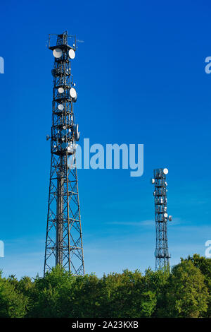 Deux mâts de télécommunication sans fil antennes TV contre blue ciel sans nuages sur green hedges Banque D'Images