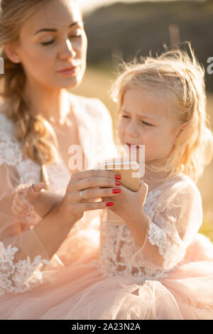 Maman donne à sa petite fille, qui pleure dans ses mains, un téléphone pour se calmer. Banque D'Images