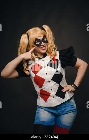 Une jeune fille dans un costume et une perruque sur un fond noir est souriant et montrant la langue. Cosplay Girl caractère Harley Quinn et s'amuser dans la salle de studio Banque D'Images