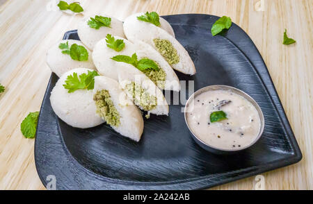 Idlis vapeur farci de viande hachée de poulet avec les feuilles de menthe avec chutney de noix de coco blanche dans une plaque noire Banque D'Images