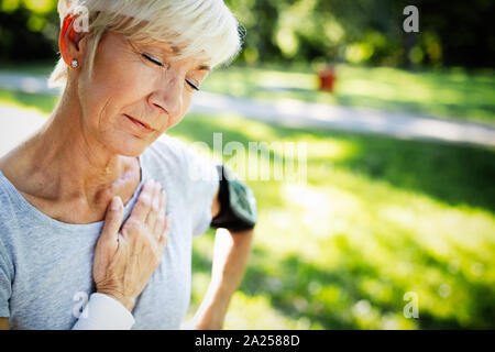 Senior woman avec douleur à la poitrine qui souffrent de crise cardiaque pendant le jogging Banque D'Images