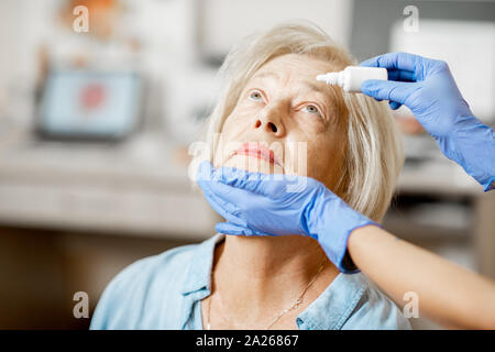 Médecin ou infirmière dans les gants des gouttes des gouttes pour les yeux sur d'un patient au cours d'un traitement à l'office d'ophtalmologie, close-up view Banque D'Images