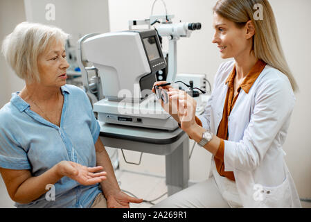 Ophtalmologue offrant lunettes pour vision d'une femme senior patient lors d'une consultation médicale dans le bureau Banque D'Images