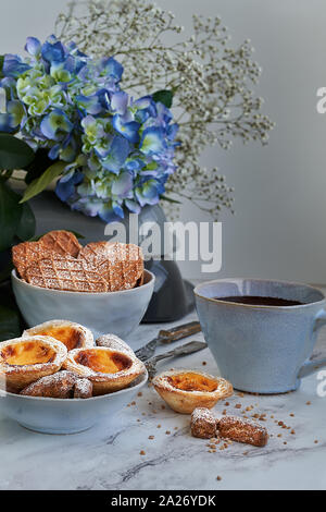 Pâte feuilletée et crème anglaise gâteaux accompagnés d'une tasse de chocolat. Arrière-plan en marbre blanc et bleu de fleurs. Banque D'Images