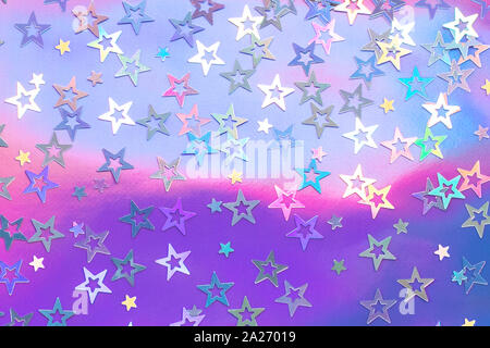 Des étoiles colorées confettis paressent sur un fond holographique tendance. Texture de vacances simple. Vue sur le dessus, plat Banque D'Images