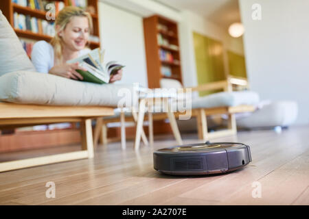 Robot Aspirateur nettoie automatiquement en marbre avec la femme au foyer dans l'arrière-plan Banque D'Images