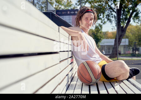 Image de l'homme sportif avec volley-ball ball assis sur banc en bois sur la journée d'été Banque D'Images