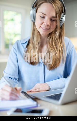 Femme étudie à la maison à l'aide d'ordinateur portable et portant des écouteurs Banque D'Images
