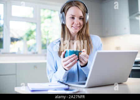 Femme étudie à la maison à l'aide d'ordinateur portable et portant des écouteurs Banque D'Images