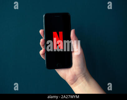 Kiev, Ukraine - 1 octobre 2019 : Studio shot of hand holding Apple iPhone 8 avec Netflix logotype sur un écran. Isolé sur un fond de papier noir. Banque D'Images