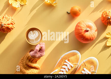 L'automne jaune le papier à plat avec la main avec tasse de pumpkin spice latte, orange citrouille, de feuilles d'érable et toile sneakers, arrangement d'automne. Banque D'Images