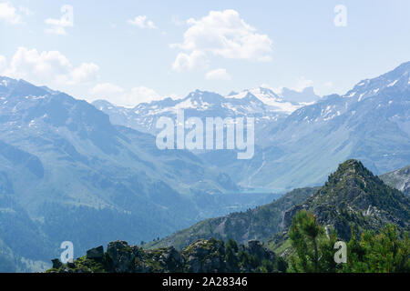 Les montagnes des Alpes couvertes de neige contre un ciel bleu avec un lac alpin dans une brume bleue en arrière-plan. Banque D'Images