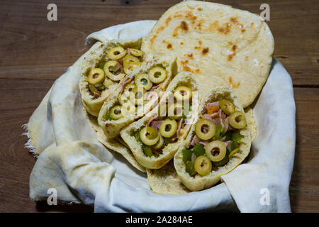 Pains plats pitta ou pita avec green olive, jambon, ail, oignon, poivron vert et tomates dans le panier en tissu, prêt à manger, sur une table en bois rustique Banque D'Images