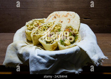 Pains plats pitta ou pita avec green olive, jambon, ail, oignon, poivron vert et tomates dans le panier en tissu, prêt à manger, sur une table en bois rustique Banque D'Images