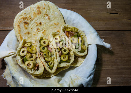 Pains plats pitta ou pita avec green olive, jambon, ail, oignon, poivron vert et tomates dans le panier en tissu, prêt à manger, sur une table en bois rustique Banque D'Images