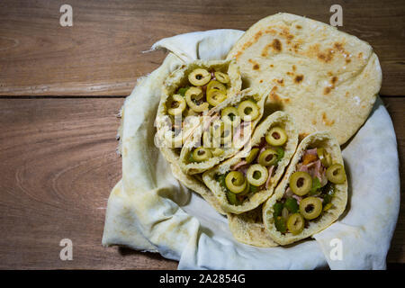 Pains plats pitta ou pita avec green olive, jambon, ail, oignon, poivron vert et tomates dans le panier en tissu, prêt à manger, sur une table en bois rustique Banque D'Images