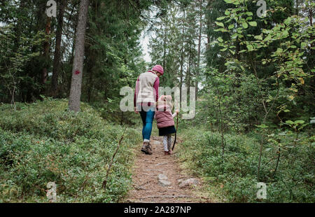 Mère tenant la main de ses filles marchant à travers la forêt en automne Banque D'Images