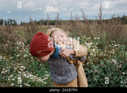 Frère portant sa sœur rire à travers un champ de fleurs sauvages Banque D'Images