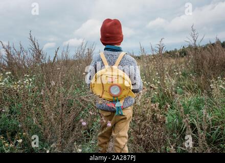 Retour d'un jeune garçon à la recherche de l'école à un champ de fleurs sauvages penser Banque D'Images