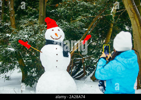 Woman taking photo de bonhomme de neige sur le téléphone Banque D'Images