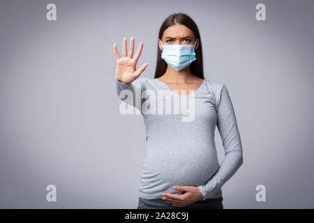 Fille enceinte dans un masque médical Gesturing Stop, Studio Shot Banque D'Images