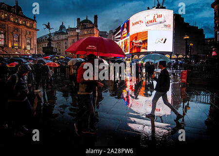 Tenir les touristes pendant une forte pluie parasols douche dans Piccadilly Circus, Londres. Banque D'Images