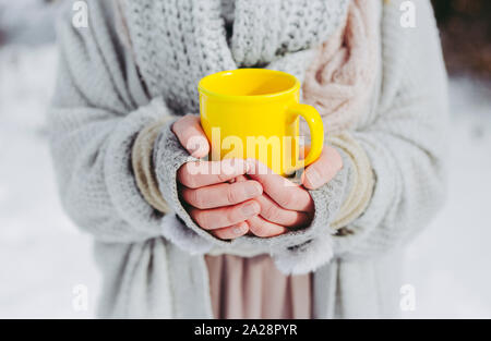 Boho fille portant doux tissé chandail est à l'extérieur en hiver et tient une tasse jaune de boisson chaude dans ses mains. Faible profondeur de champ. Banque D'Images
